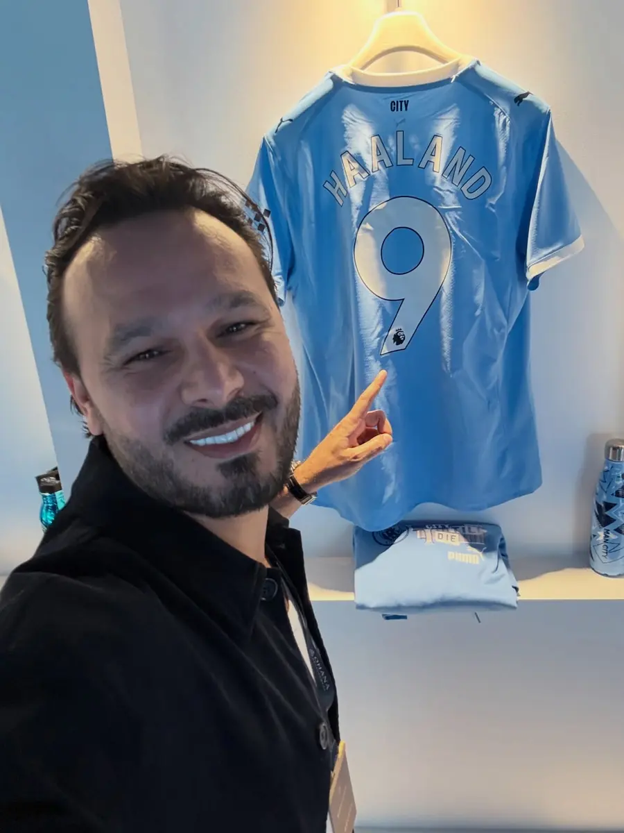 Ayoub smiling beside a signed Manchester City shirt