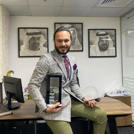 Ayoub at his desk with an award plaque